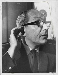 1968 Fred Lagone wearing dark rimmed glasses with hand on ear Press 