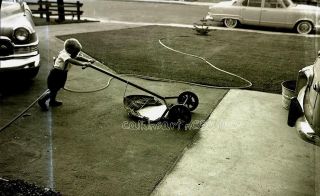 NEGATIVE Young boy pushing lawn mower, framed by big cars 1950s