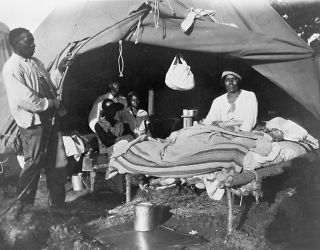 Americans in front of tent, with one man sitting up on bed, duri c6