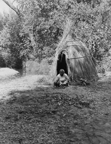 c1924 photo Pomo Indian woman cooking in front of cane tepee